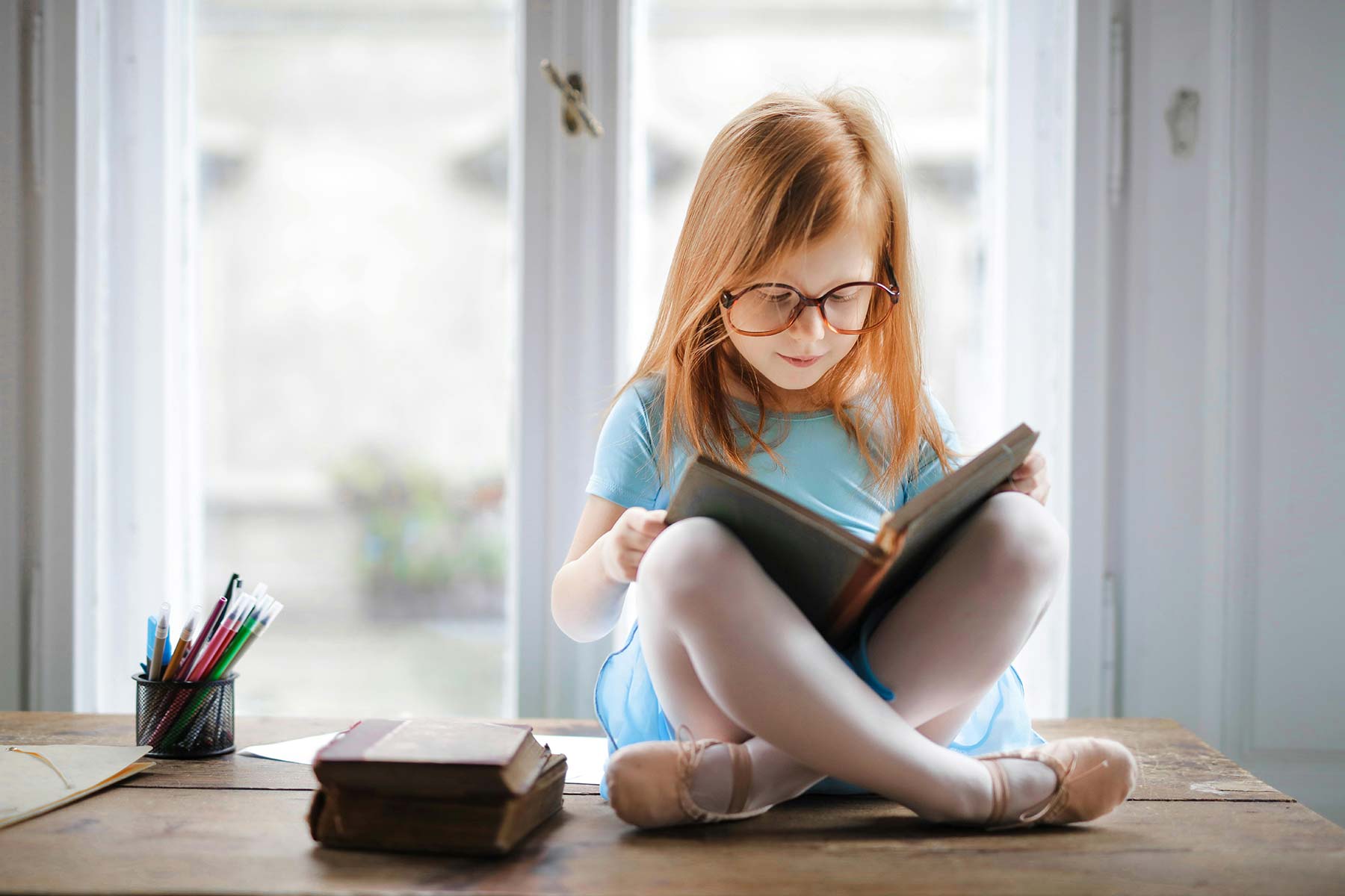 A little girl wearing ballet slippers reading a book