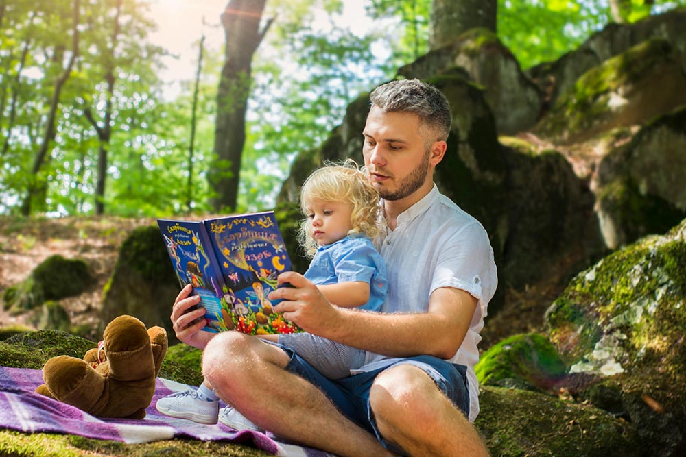 Man reading to his child outdoors during the day in nature
