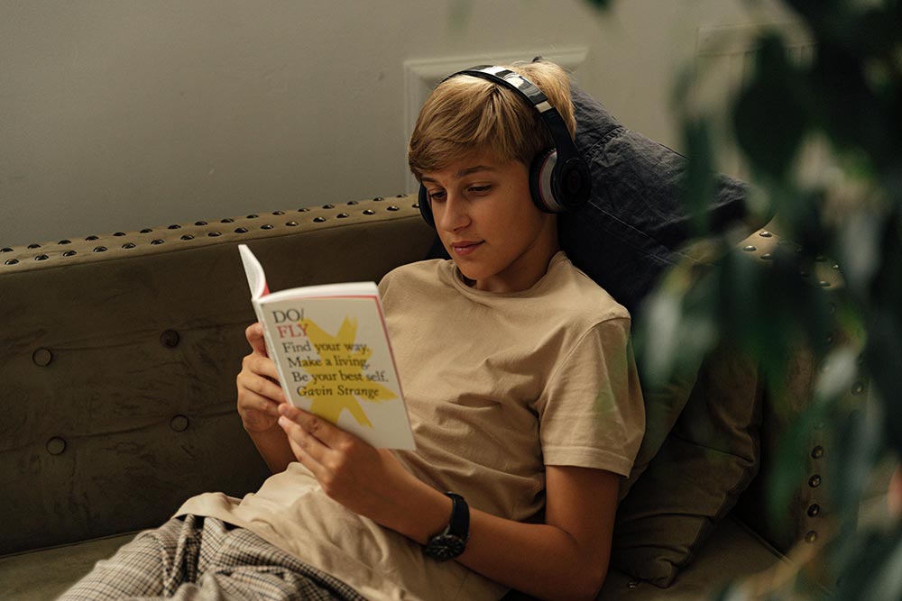 Teen boy reading on a couch while wearing headphones