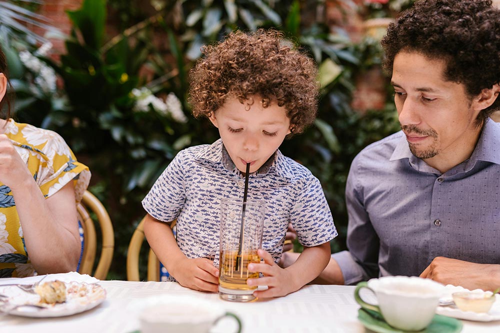 Young boy at a table drinking from a straw with his dad looking on 